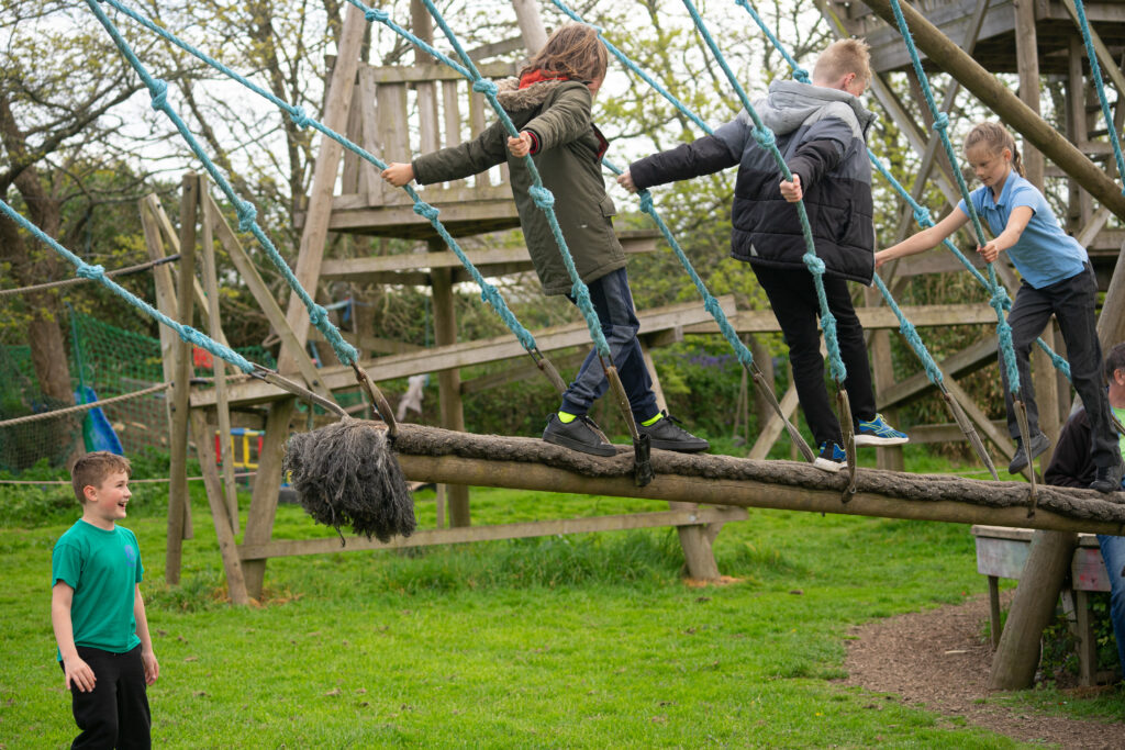 Children playing on the dragon swing. A long piece of wood surrounded by rope suspended from a frame to swing back and forth.